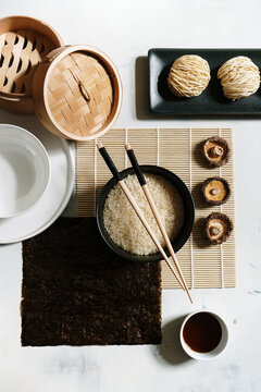Top view of rice in bowl with wooden chopsticks arranged on table with soy sauce and dry noodles