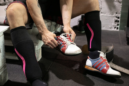 Cropped unrecognizable athletic male weightlifter putting on sport shoes before workout in modern gym