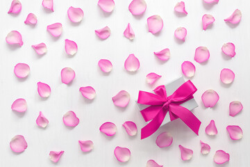 Pattern of pink rose petals and gift box with bright pink ribbon. White painted old wooden background. Valentine's Day. Top view, flat lay.