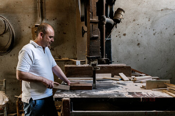 Talented male woodworker using band saw for cutting wooden plank in grungy workshop