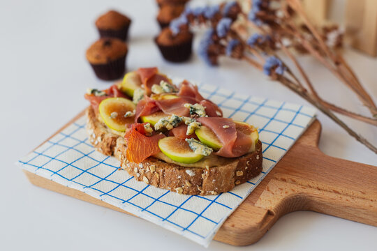 Appetizing homemade sandwich made with wholegrain bread toast and fresh sliced fruit with ham served for breakfast on wooden board