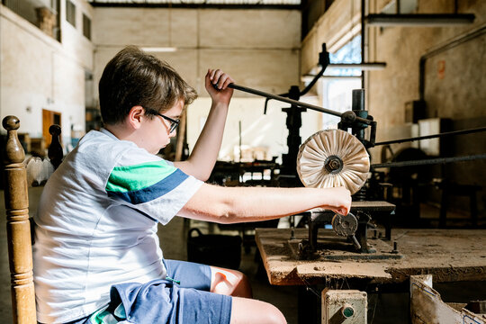 Focused teenage boy working with old drill press while polishing detail in workshop