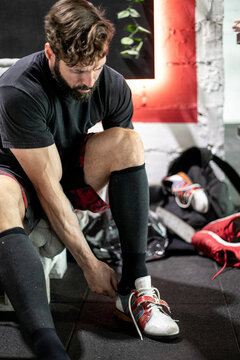 Focused athletic male weightlifter putting on sport shoes before workout in modern gym