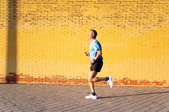 Senior retired man running through the city on yellow background