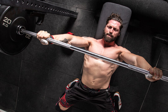 From Above Of Strong Focused Male Athlete Lying On Bench Press And Doing Exercises With Heavy Barbell During Workout In Gym