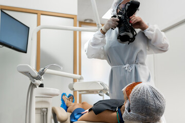 Unrecognizable professional dentist using portable X ray device for examining teeth of patient in protective goggles while working in modern dental clinic