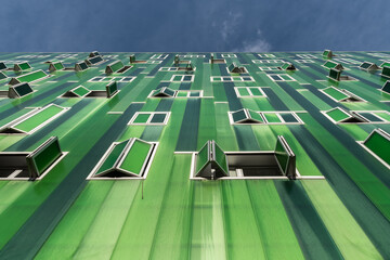 From below contemporary building with vivid green facade and opened windows on blue sky