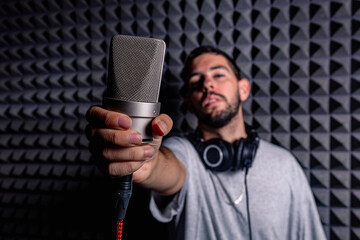 Talented male singer with modern microphone standing in acoustic soundproof room in music recording studio and looking at camera