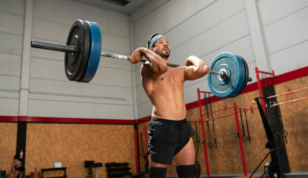 From below of concentrated male athlete lifting heavy barbell during weightlifting workout in gym while looking away