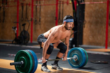 Concentrated male athlete lifting heavy barbell during weightlifting workout in gym while looking away
