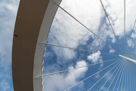 From below of part of futuristic suspension bridge with solid steel cables on background of blue cloudy sky