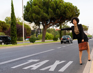 Full body of confident African American female worker in classy wear waving hand for taxi while standing on road
