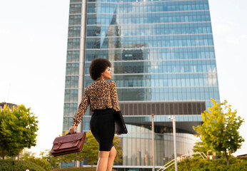 Back view of well dressed African American female worker carrying bag while strolling in business district
