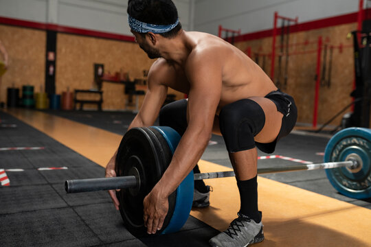 Side view of muscular male athlete with naked torso preparing heavy barbell for intense weightlifting workout while looking away