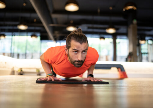 Bearded adult sportsman doing push-ups during fitness training in contemporary gym