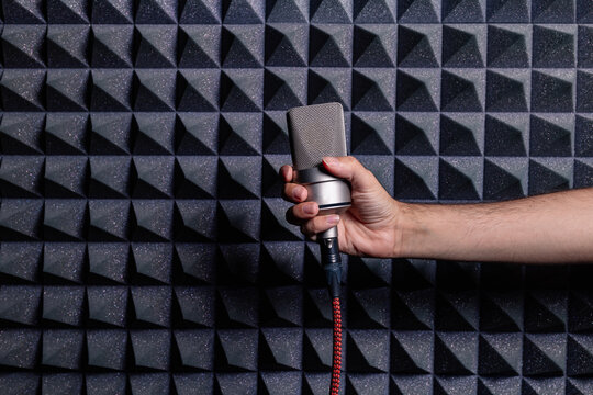 Unrecognizable crop male artist standing with modern wired microphone in recoding studio on background of acoustic panel with soundproof foam