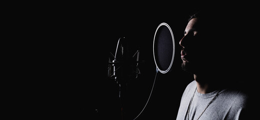 Talented male singer recording music in front of modern microphone in dark studio