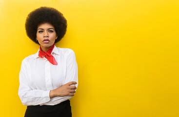 Confident African American female in elegant formal outfit standing with arms crossed against yellow background