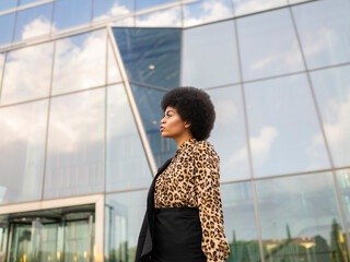 Confident African American female in formal wear standing near modern office building in downtown