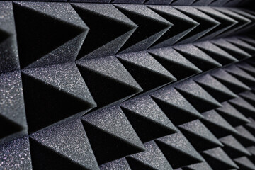 Textured background of wall with black geometric soundproof foam with pyramid shaped pattern in recording studio
