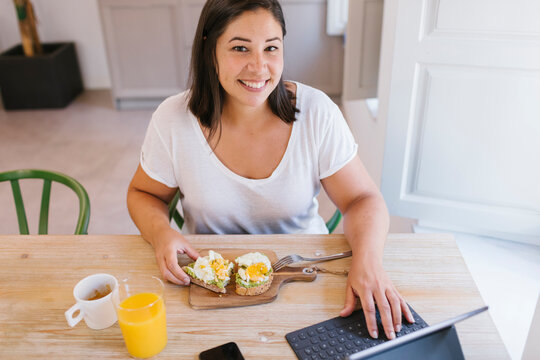 Happy smiley woman having a healthy breakfast and working from home with a tablet