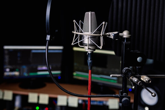 Contemporary metal microphone with wire placed in dark music recording studio on blurred background of computer monitors