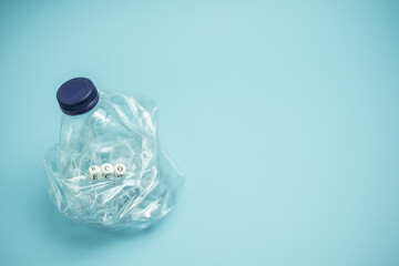 Crumpled plastic bottle placed on blue background in studio demonstrating concept of waste recycling