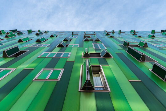 From below contemporary building with vivid green facade and opened windows on blue sky