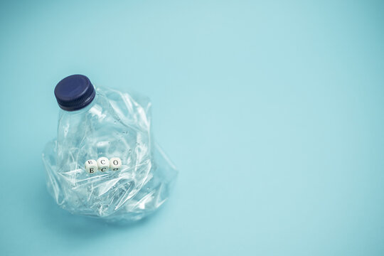 Crumpled plastic bottle placed on blue background in studio demonstrating concept of waste recycling