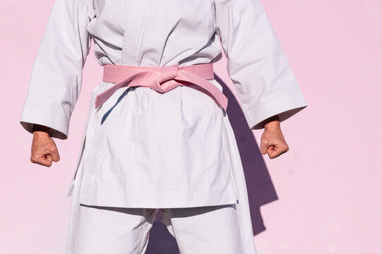 Cropped unrecognizable determined mature woman in pink head cover and belt fighting karate in cancer battle concept in the street on pink wall