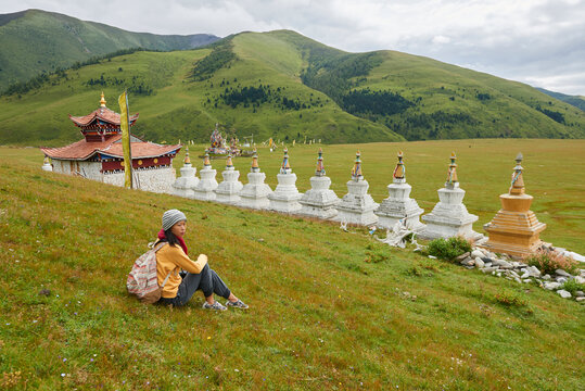 Side view full length of Asian female backpacker enjoying vacation near oriental shrine located in green valley in China