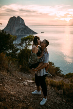 Side view of passionate couple hugging and kissing while standing on hill on background of sunset over sea
