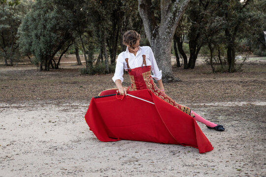 Slim focused male bullfighter in red pants and white shirt holding cloak performing gracefully before corrida in nature