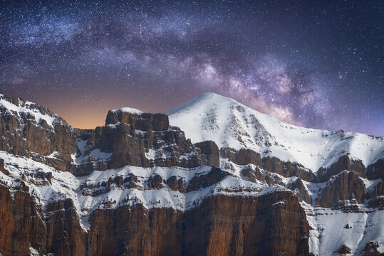 Spectacular view of high rough ridge covered with snow under colorful starry sky during milky way phenomenon