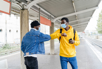 Side view of cheerful African American friends in medical masks bumping elbows while greeting each other during COVID 19 epidemic