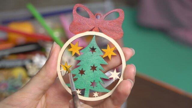 Decorate the Christmas ball. Paint the Christmas tree toy with colors. Create a decoration for the new year at home. Hobbies and creativity, handmade. The artist draws on a wooden toy. Art, creation.