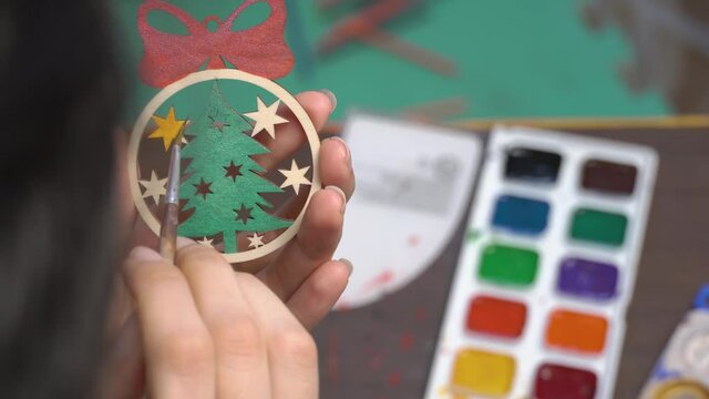 The artist draws on a wooden toy. Paint the Christmas tree toy with colors. Create a decoration for the new year at home. Hobbies and creativity, handmade. Art, creation. Decorate the Christmas ball