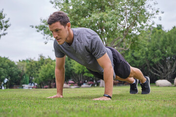 Low angle of strong male athlete doing push ups during training on green lawn in park
