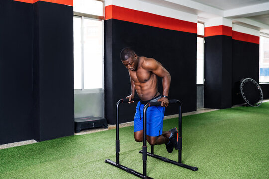Concentrated African American male athlete doing exercises on parallel bars while pumping triceps during workout in gym
