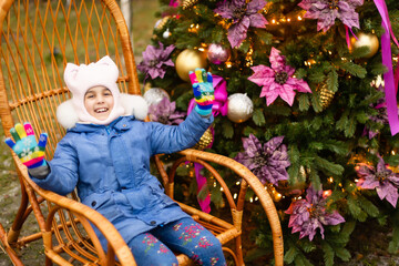 little girl in rocking chair near christmas tree on the street