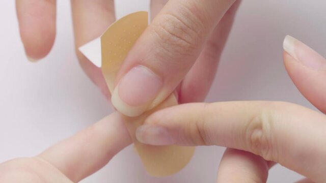 Apply a patch on the child's finger. Mother hands applying antibacterial medical adhesive plaster on child's finger after wounding at home. First aid for kids after injury. Medical care for a child.