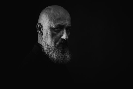 close up photo, portrait of a serious, thoughtful, bearded man on a dark background confident and dramatic looking straight. Concept of male portrait. Black and white photo. Low key