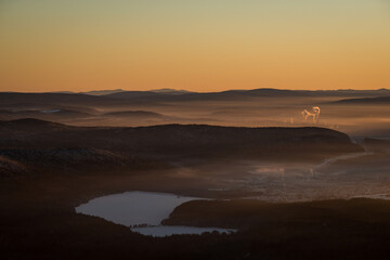 the sun sets below the horizon and illuminates the fog hovering over the city in the mountains