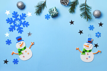 A child is making a Christmas present with a snowman. Christmas tree hanging ornaments. Snowman parts on blue wooden background.