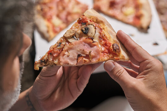 Overhead view of cropped unrecognizable males enjoying delivered appetizing pizza while resting on carpet at home