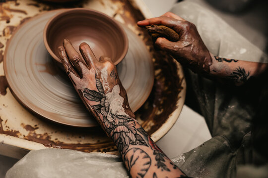 Closeup of dirty hands of anonymous craftsman using pottery wheel and making clay pot in workshop