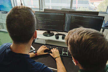 Back view high angle of unrecognizable male programmer developing software together while typing on keyboard and working in modern office