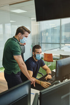From above of male coworkers in medical masks together using program for software during coronavirus pandemic