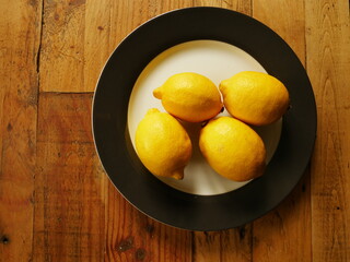 View from above on four lemons resting on a plate on a wooden background