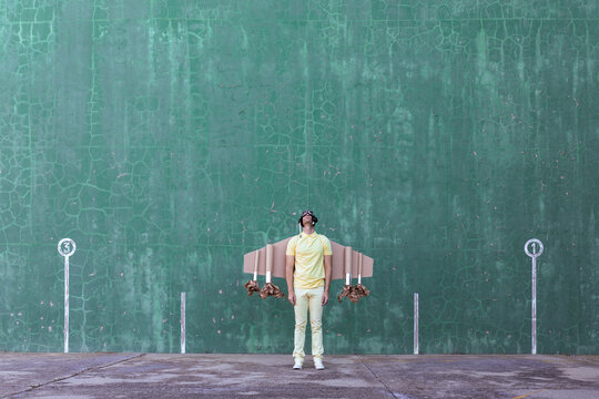 Male in handmade cardboard wings standing looking up while dreaming about achieving success